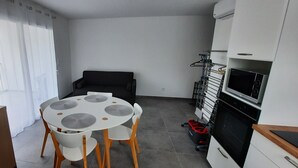 A compact living space with a dining table, chairs, a sofa, a kitchenette, and a TV.