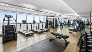 A modern gym with treadmills, weight machines, and a large window offering a city view. - Charming Studio in Saba 3, Jumeirah Lake Tower by Deluxe Holiday Homes (Dubai)