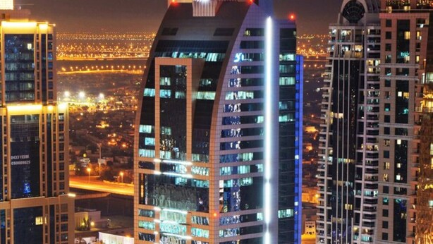 A high-rise building with a curved facade, multiple floors, and a parking area in front. - Charming Studio in Saba 3, Jumeirah Lake Tower by Deluxe Holiday Homes (Dubai)