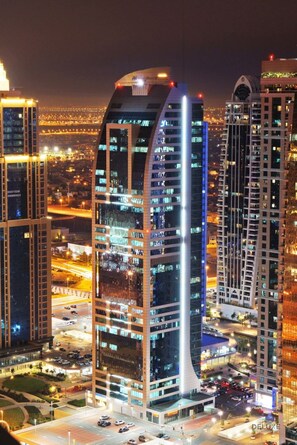 A high-rise building with a curved facade, multiple floors, and a parking area in front. - Charming Studio in Saba 3, Jumeirah Lake Tower by Deluxe Holiday Homes (Dubai)