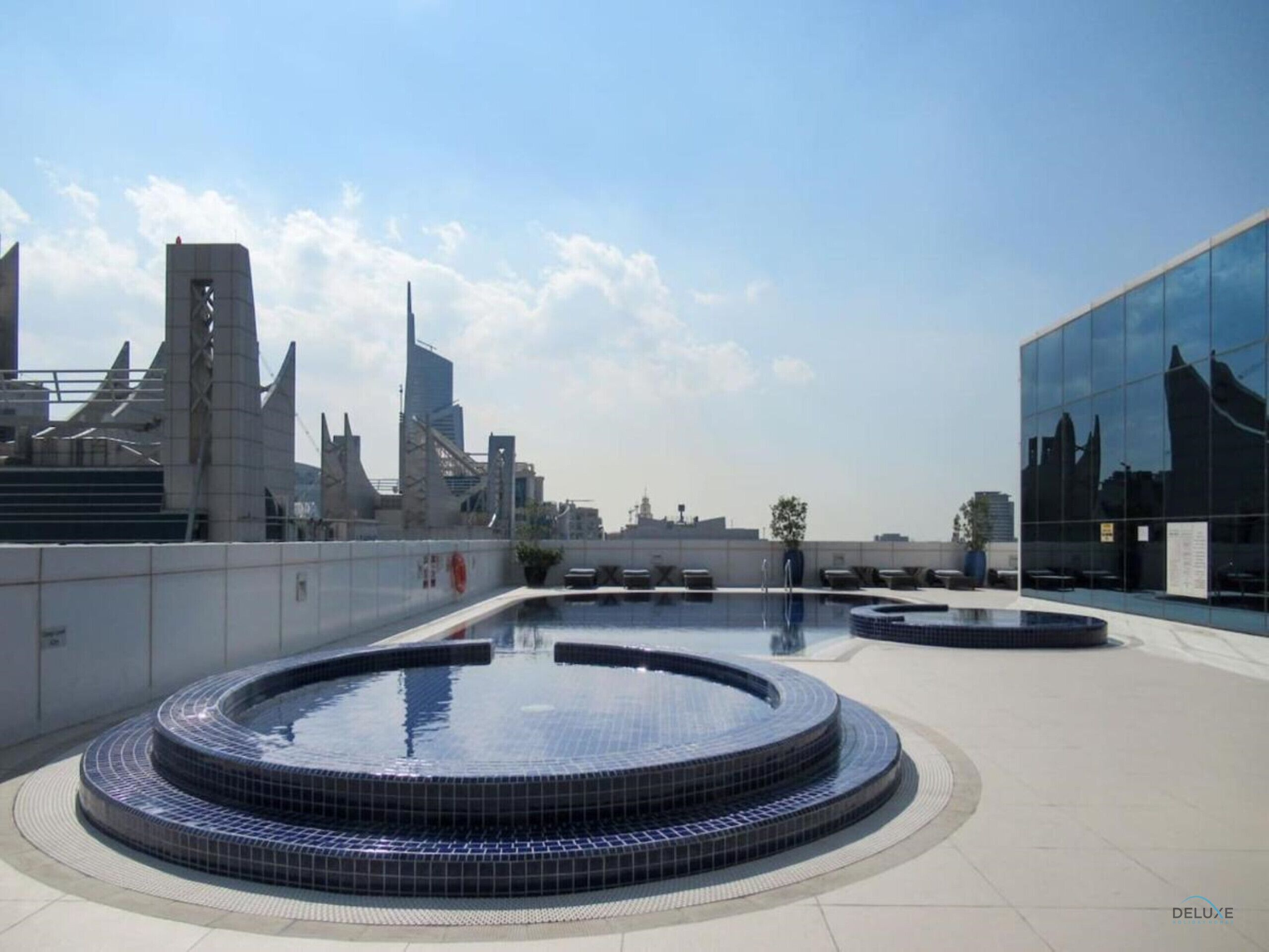 Un área de piscina en la azotea con un diseño circular, rodeada de edificios modernos y un cielo despejado.