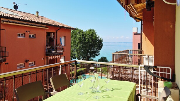 Un balcón con una mesa lista para comer, con vista a una piscina y al mar.