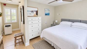 Un dormitorio con cama, cómoda, mesita de noche, ventilador de techo y ventana con persianas.