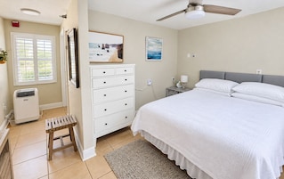 A bedroom with a bed, a dresser, a nightstand, a ceiling fan, and a window with blinds.