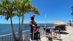 Una estatua de pirata en un muelle con palmeras, asientos al aire libre y vistas al agua.