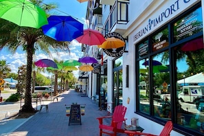 A storefront with colorful umbrellas, a sign reading "IBERIAN IMPORT CO.", and a sidewalk with chairs and a chalkboard sign.