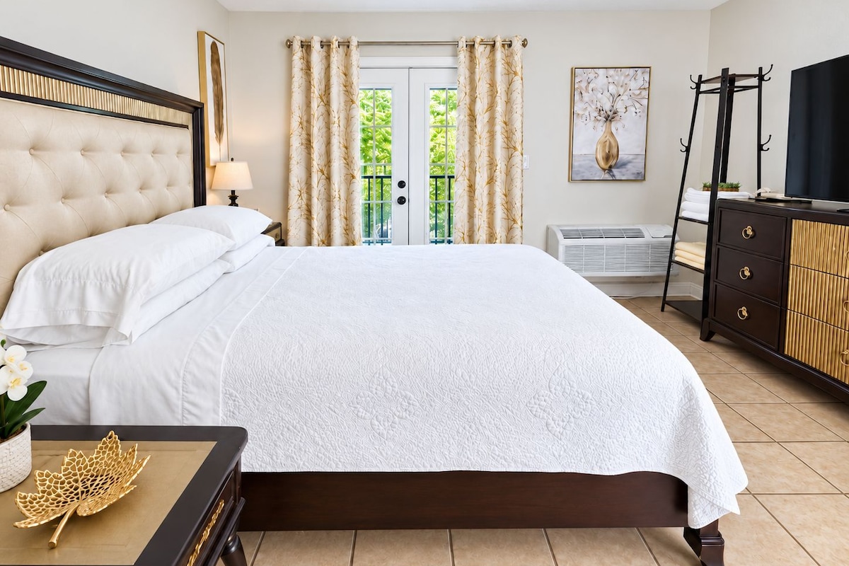A hotel room with a large bed, a bedside table with a lamp, a dresser, and a television.