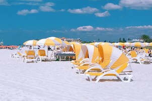 Una playa con hileras de sillas y sombrillas a rayas blancas y amarillas, dispuestas en línea.