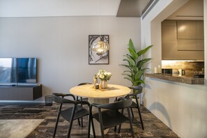 Un área de comedor moderna con una mesa redonda, sillas negras, un jarrón con flores, una lámpara colgante y una encimera de cocina con una cafetera.