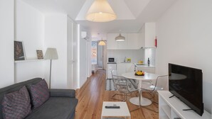 A modern living room with a sofa, a TV, and a dining area with chairs and a table.