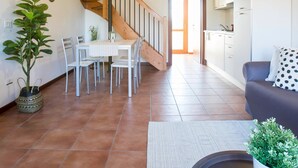 Ein geräumiger Wohnbereich mit einer Holztreppe, einem Esstisch mit Stühlen, einer Couch und einem Topfpflanzen.