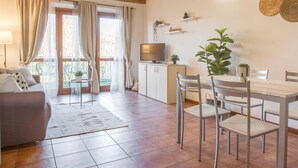Ein gemütliches Wohnzimmer mit einer Couch, einem Esstisch, Stühlen, einem Fernseher und einem Balkon mit Vorhängen.