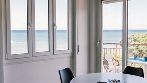 Een kamer met een ronde tafel, twee stoelen en uitzicht op de zee door grote ramen.