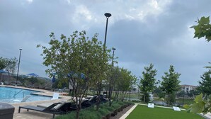 Uma piscina com espreguiçadeiras, uma pequena área gramada com um banco e uma cerca delimitando o espaço.