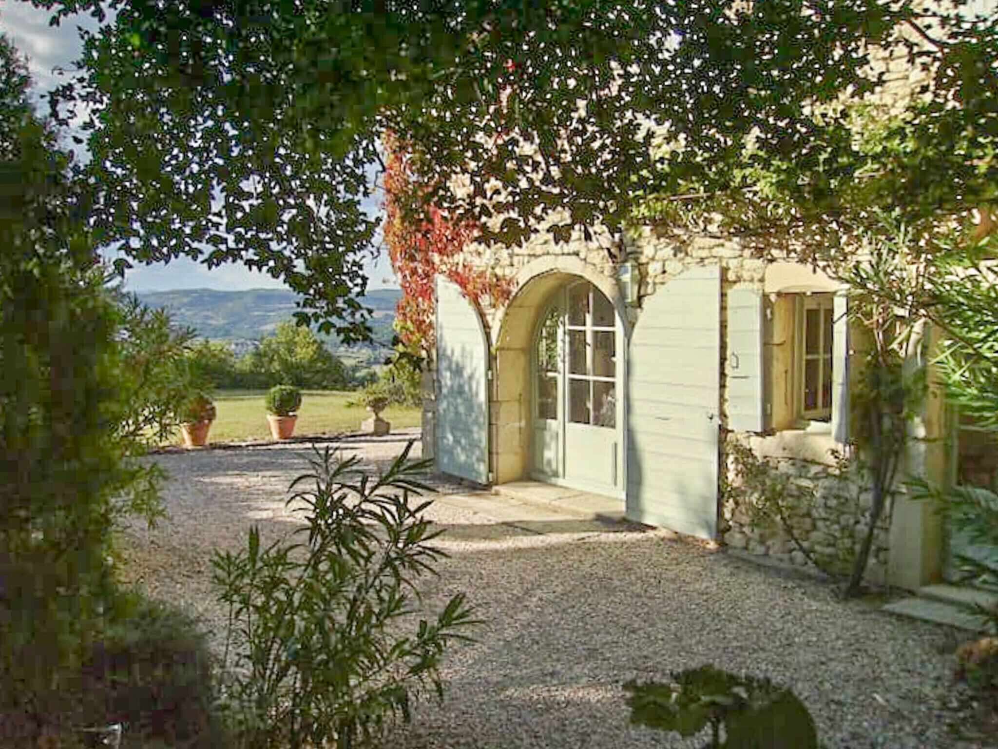 A rustic stone building with an arched entrance, a gravel driveway, and potted plants.