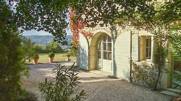 A rustic stone building with an arched entrance, a gravel driveway, and potted plants.