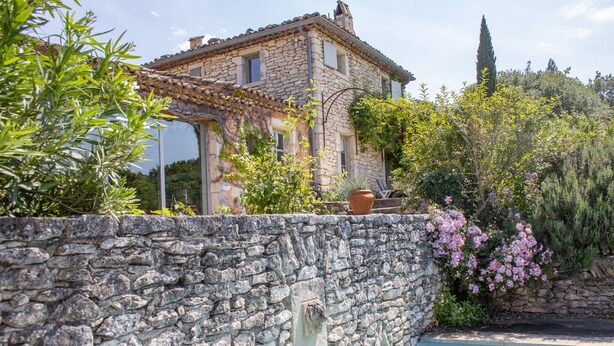 Una casa de piedra con piscina, rodeada de exuberante vegetación y plantas en flor.
