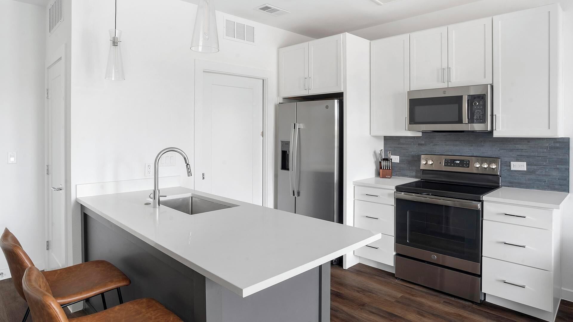 A modern kitchen with white cabinetry, stainless steel appliances, a central island with a sink, and a wooden chair.