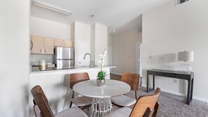 A modern kitchen with white cabinets, a stainless steel refrigerator, and a dining area with a round table and chairs. - Landing | Amazing 1BD, Clubhouse, Pool (Memphis)