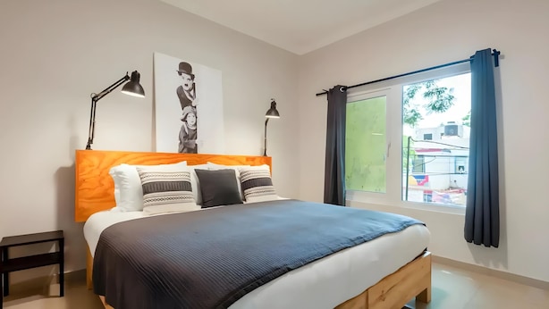 Een slaapkamer met een houten bed, twee bedlampen, een groot raam met gordijnen en een kunstwerk aan de muur.