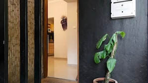Een hal met een potplant, een lichtschakelaar aan de muur en een deur die leidt naar een keuken.