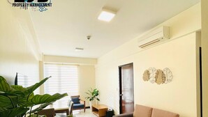 A spacious living room with a sofa, a dining area with a table and chairs, and a large potted plant. - Mactan Newtown by EJB (Lapu-Lapu City)