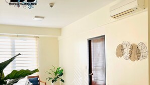 A modern living room with a sofa, a wooden coffee table, and a potted plant. There is a door with a decorative leaf pattern on the wall. - Mactan Newtown by EJB (Lapu-Lapu City)