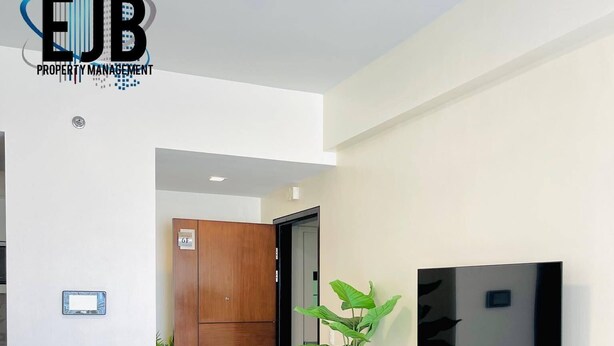 A modern hotel lobby with a flat-screen TV mounted on the wall, a wooden cabinet with a remote control, and a potted plant. - Mactan Newtown by EJB (Lapu-Lapu City)