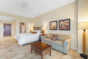 A hotel room with a bed, a sofa, a coffee table, two wall-mounted lamps, and two framed artworks.