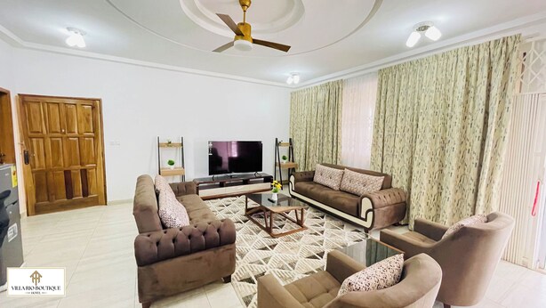 A living room with a sofa set, a coffee table, a TV, and a ceiling fan. - Villa Rio Boutique Hotel (Atimpoku)