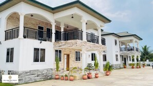 A multi-story hotel with a white facade, multiple balconies, and potted plants. - Villa Rio Boutique Hotel (Atimpoku)