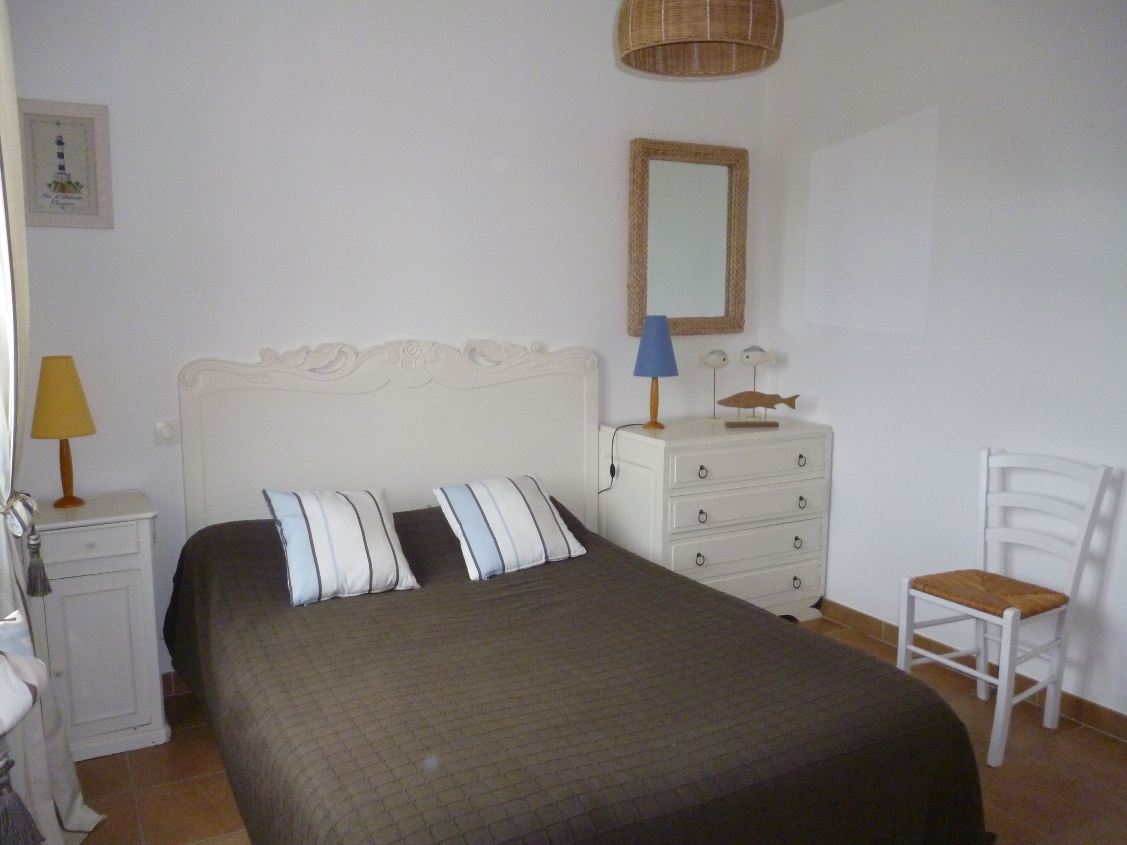 Un dormitorio con cama, cómoda, silla, lámpara y espejo montado en la pared.