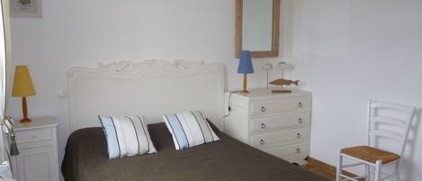 Un dormitorio con cama, cómoda, silla, lámpara y espejo montado en la pared.