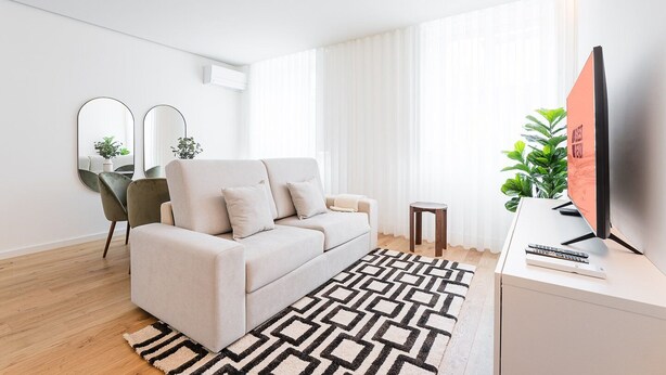 A modern living room with a beige sofa, a patterned rug, a small side table, and a TV on a stand. - GuestReady - A marvellous city retreat (Porto)