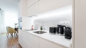 A modern kitchen with white cabinets, a marble countertop, a sink, a toaster, a coffee maker, and a dining area with chairs and a table. - GuestReady - A marvellous city retreat (Porto)