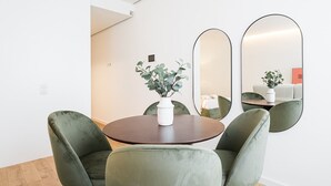A modern hotel room with a round dining table, two green upholstered chairs, a white vase with a plant, and three large mirrors on the wall. - GuestReady - A marvellous city retreat (Porto)