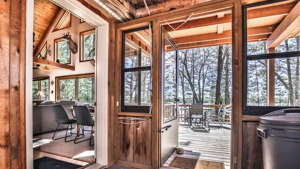 A cabin interior with a dining area, a large window, and a deck with outdoor seating.
