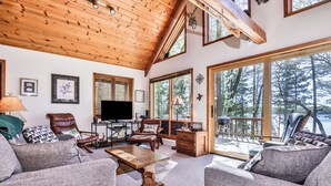 A cozy living room with a fireplace, comfortable seating, and large windows offering a view of the outdoors.