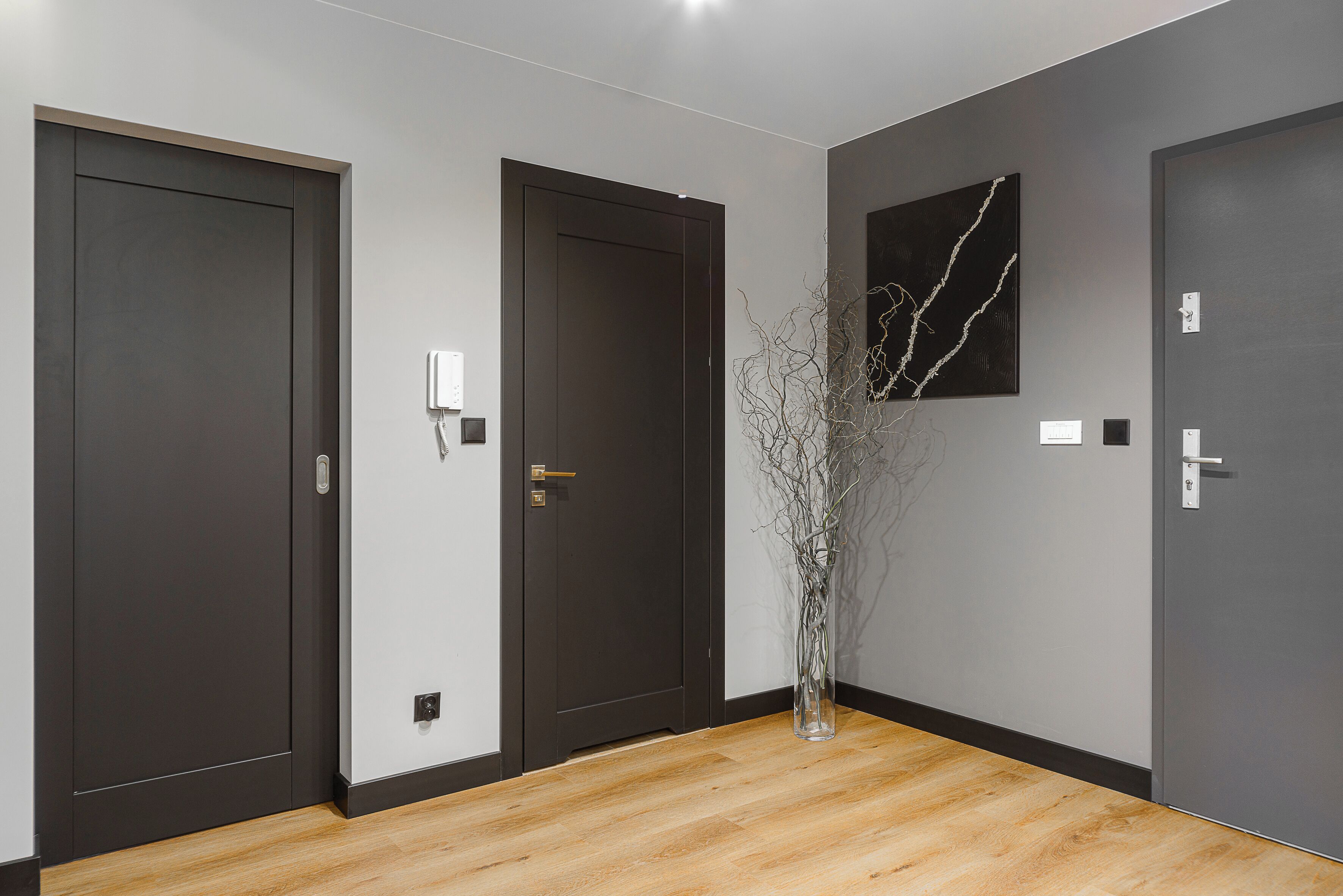 A hallway with three dark doors, a vase with branches, and a marble-patterned wall art piece.