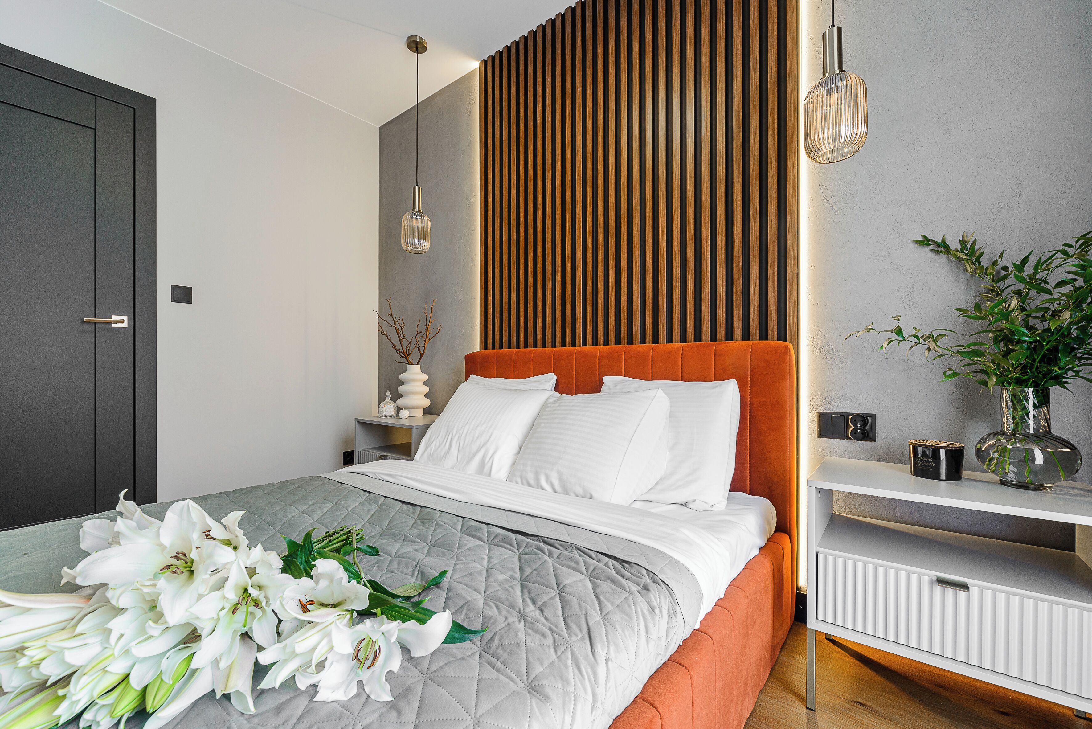 Un dormitorio moderno con una cama, una mesita de noche, un estante en la pared y una puerta.