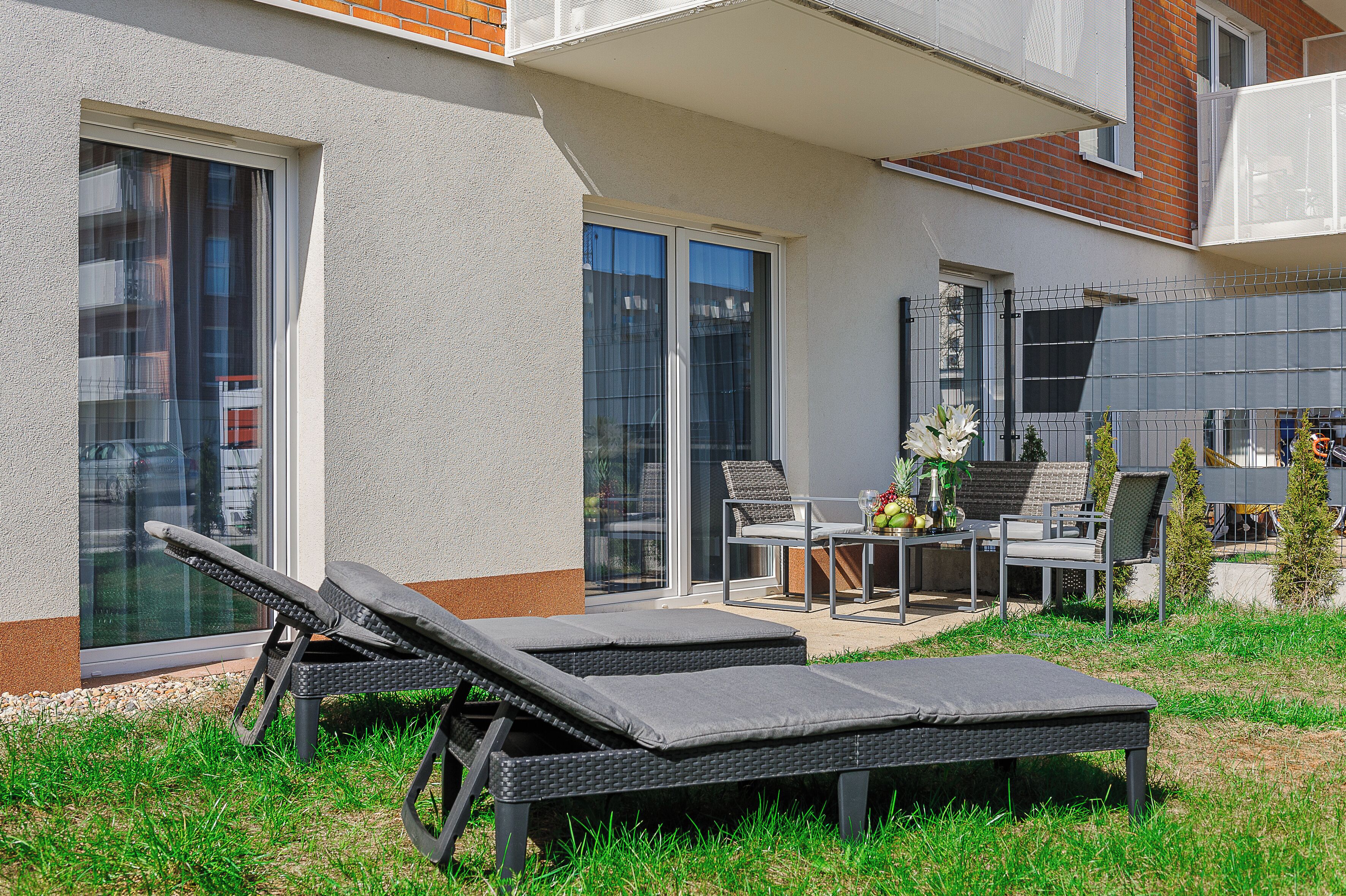Un patio extérieur moderne comprenant deux chaises longues, une table avec des chaises et un petit espace aménagé en jardin.