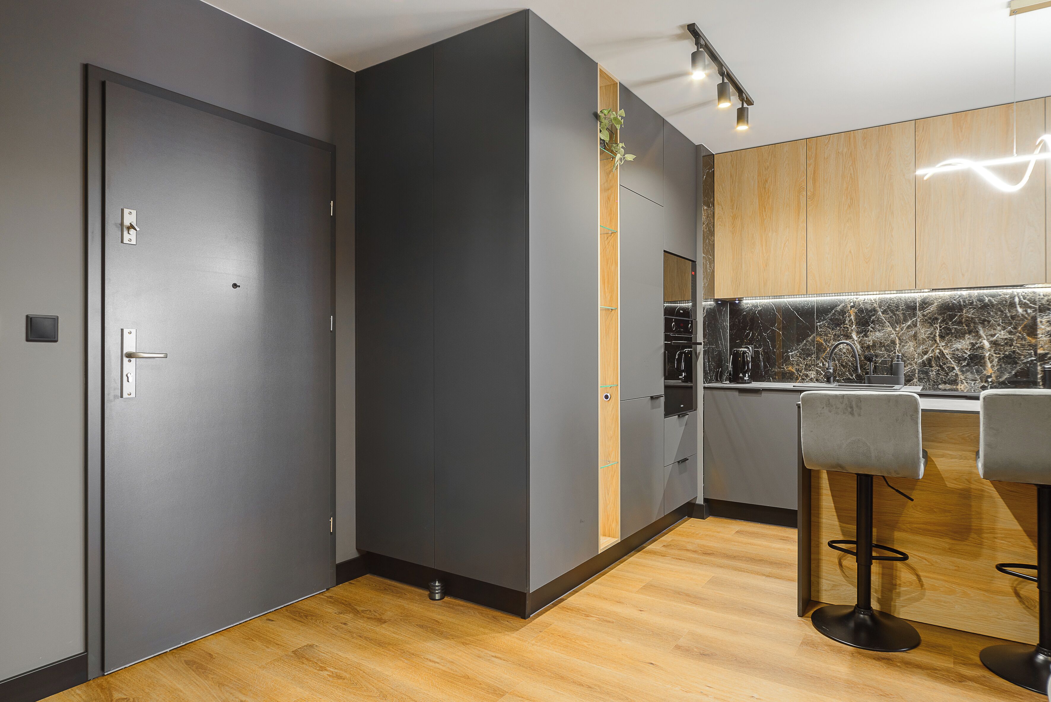 A modern kitchen with grey cabinets, wooden flooring, and two bar stools.