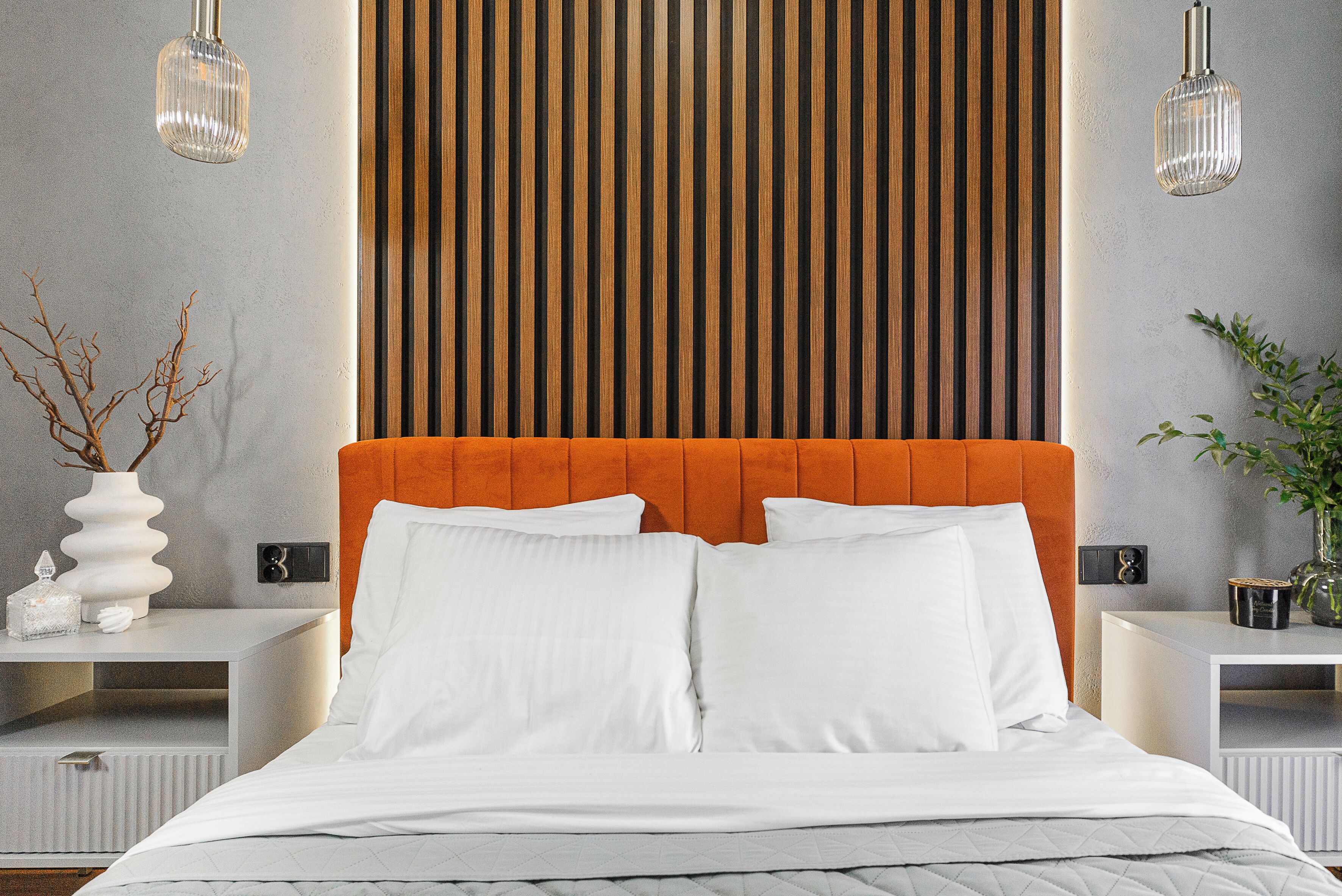 Une chambre à coucher moderne avec un grand lit, une tête de lit en lattes de bois et deux tables de chevet avec des lampes.