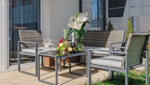 Een terras met een tafel gedekt voor twee personen, met rieten stoelen en een fruitschaal met ananas en appels.