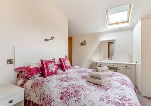 Relax in this serene bedroom with a large bed, bedside table, and dresser, featuring a floral-patterned bedspread and matching pillows.