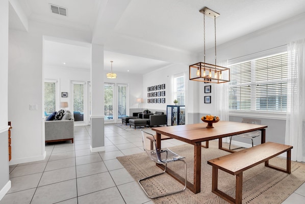 A spacious living area with a wooden dining table, benches, and a modern chandelier.