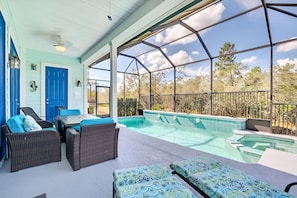 A covered outdoor area with a swimming pool, wicker furniture, and a blue door.