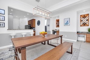 A modern kitchen with a wooden dining table, a fruit bowl, and a hanging light fixture.