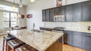 A modern kitchen with dark cabinets, a granite island, stainless steel appliances, and pendant lighting. - Houston Home w/ Rooftop Patio - 3 Mi to Downtown!
 (Houston)