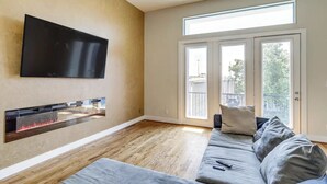 A living room with a flat-screen TV mounted on the wall, a built-in fireplace, a grey sofa, and a large sliding glass door leading to a balcony. - Houston Home w/ Rooftop Patio - 3 Mi to Downtown!
 (Houston)
